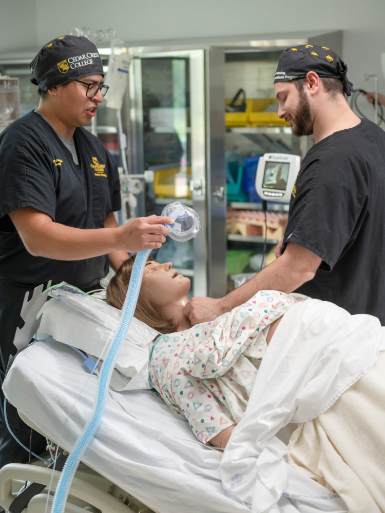 Two healthcare workers fit a breathing mask on a patient lying in a hospital bed.