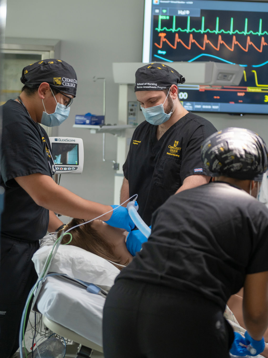 Anesthesia team intubating a patient on an operating table, with a ventilator bag and vital-sign monitor in the background.