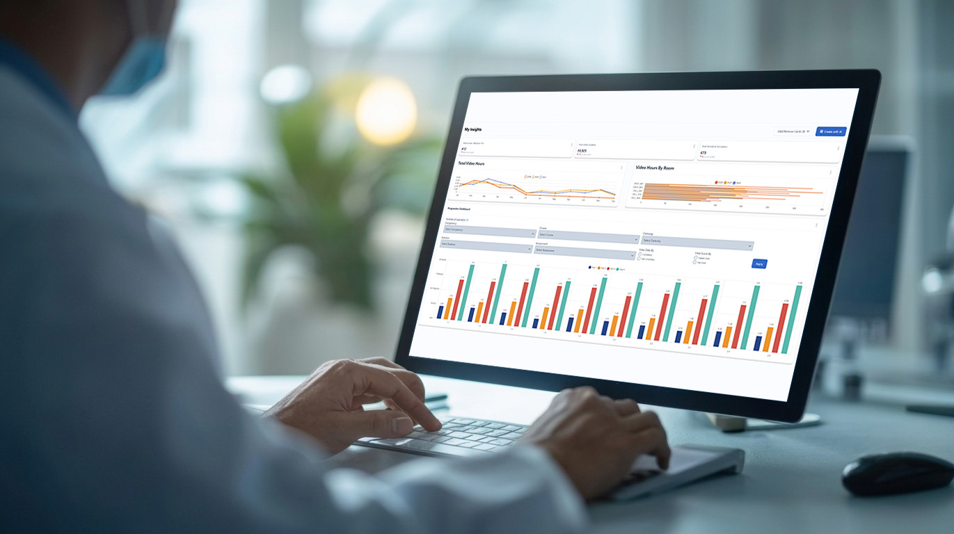 Person in a white coat at a desk viewing a monitor that displays a data analytics dashboard with charts and graphs to interpret information.